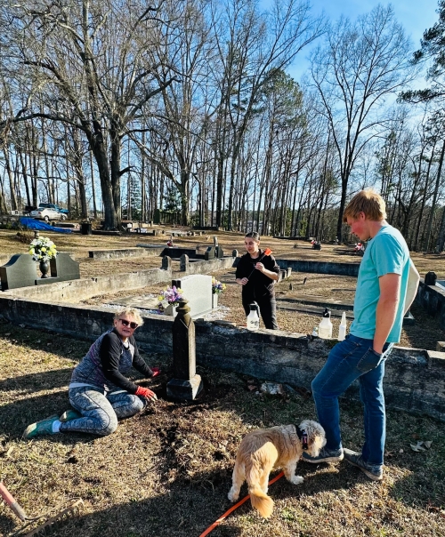 Gail Jenkins, President of Friends of the Historic Fayetteville Cemetery, digging out the base of this headstone that has been buried due to years of neglect. Jennifer Sarlo and Jacob Morgan looking on Photo by Joey Morgan ©2024